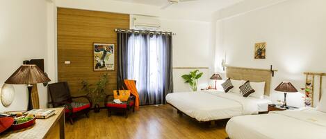 A hotel room with two beds, a desk, a chair, a table with a lamp, and a ceiling fan.