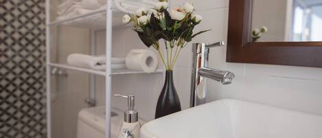 A bathroom with a white sink, a mirror, and a shelf with towels and toiletries.