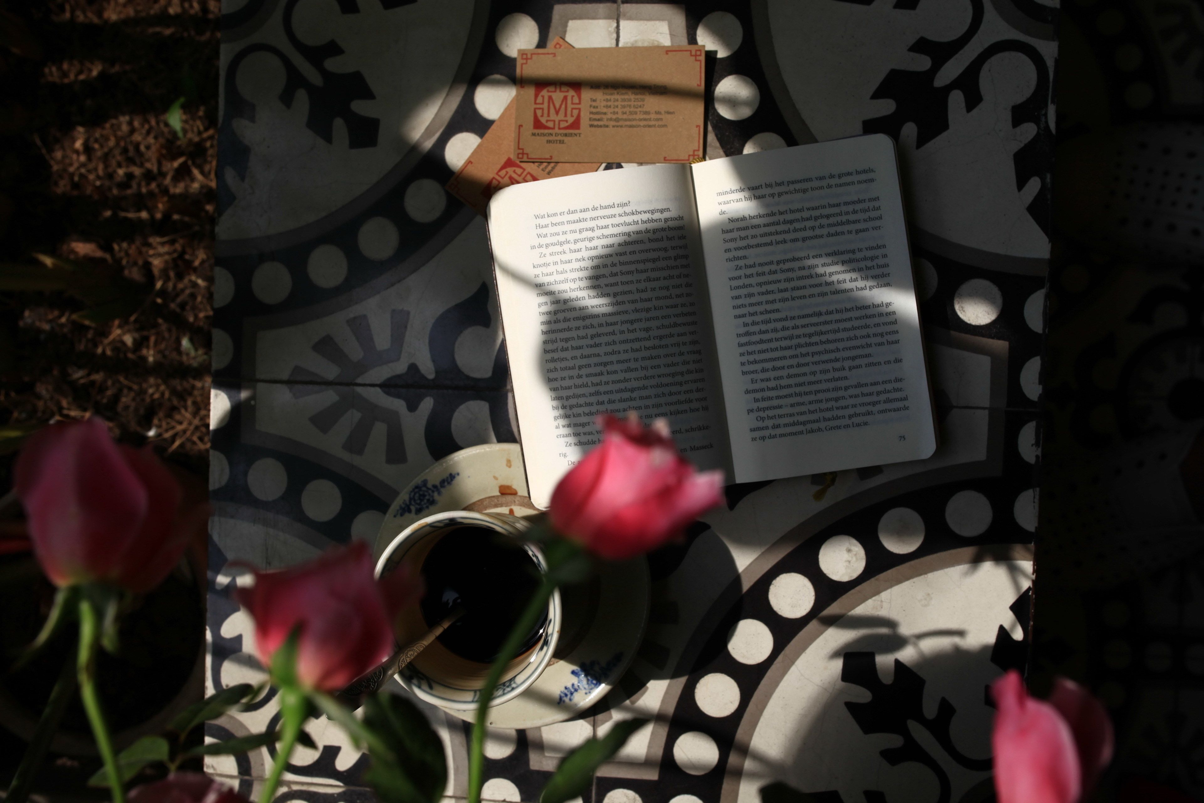 Un libro, una taza y una rosa sobre una mesa estampada.