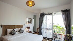A hotel room with a large bed, a bedside table with a lamp, a chair, and a view of the outdoors through a sliding glass door. - Maison d'Orient Hotel (Hanoi)