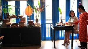 A room with a dining table, chairs, a kitchen counter with various items, and large windows with blue curtains. - Maison d'Orient Hotel (Hanoi)