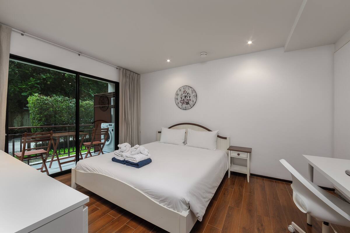 Une chambre d’hôtel moderne dotée d’un grand lit, d’un bureau et d’un balcon offrant une vue sur la verdure.