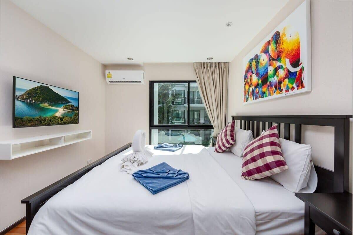Une chambre d’hôtel avec un lit, un téléviseur fixé au mur, une fenêtre avec des rideaux et un tableau accroché au mur.