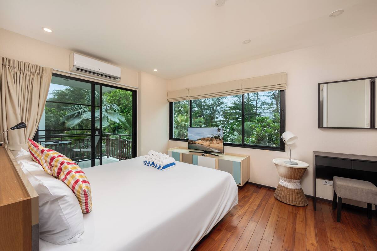 Une chambre d’hôtel moderne, dotée d’un grand lit, d’une télévision, d’un petit bureau et offrant une vue sur la verdure environnante.
