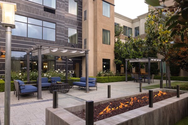 Een terras met moderne meubels, een vuurplaats en een gebouw met grote ramen op de achtergrond.