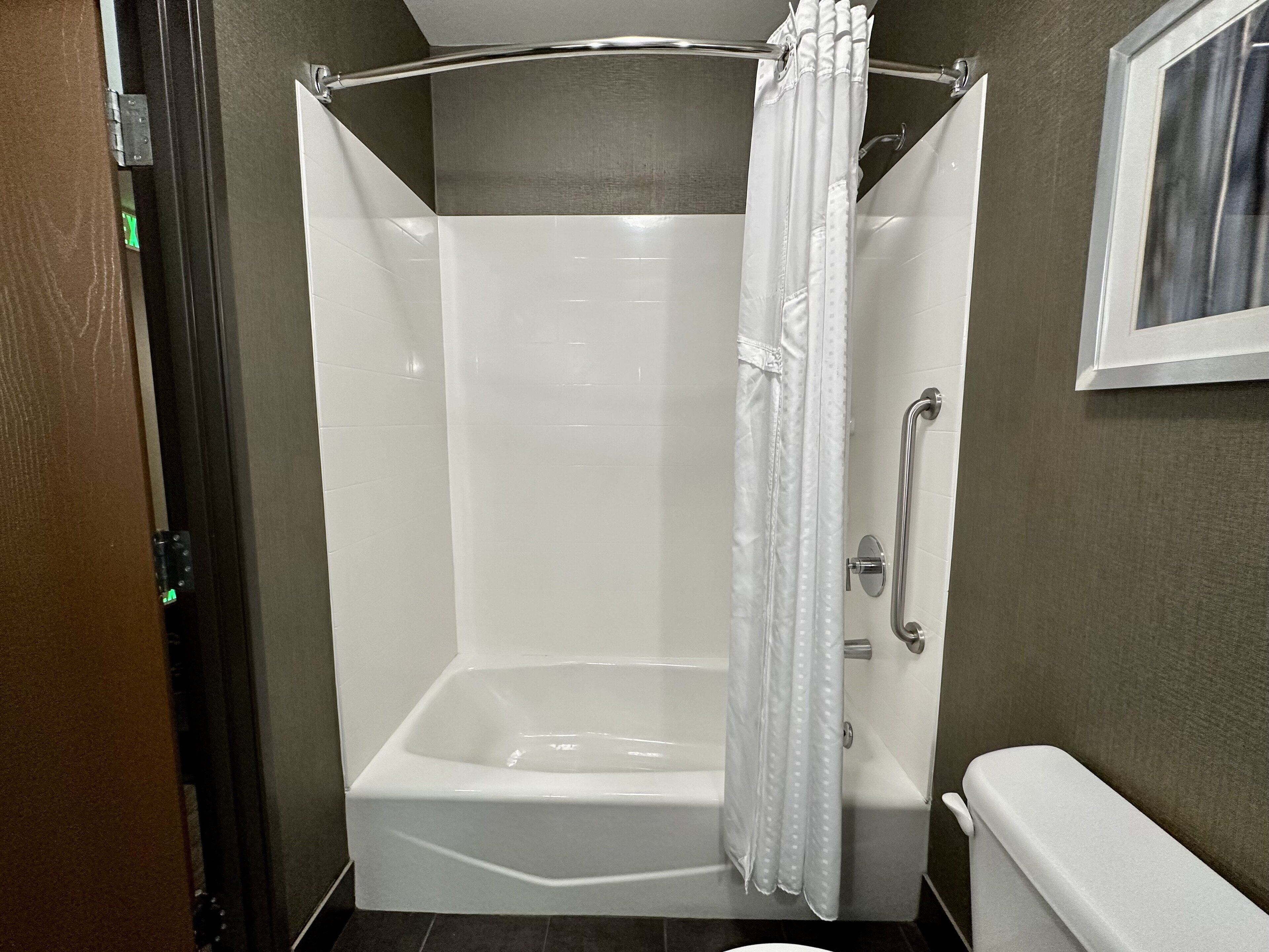 Una ducha a nivel con una bañera blanca, una cortina de ducha y una barra de apoyo.