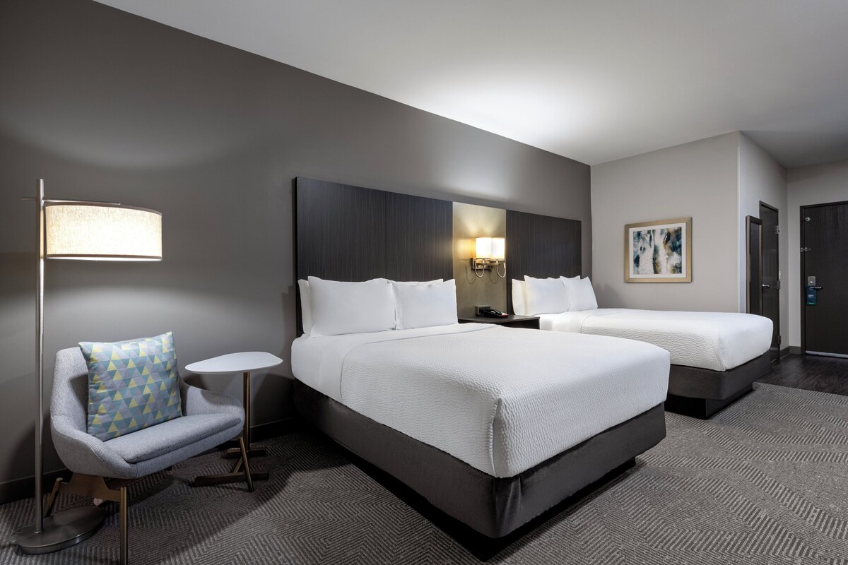 Een hotelkamer met twee bedden, een bank, een lamp, een nachtkastje en een schilderij aan de muur.