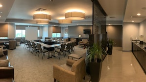 A spacious conference room with a large table, multiple chairs, and a sofa. There are ceiling lights, a television, and a kitchen area visible. - Holiday Inn Carlsbad by IHG (Carlsbad)