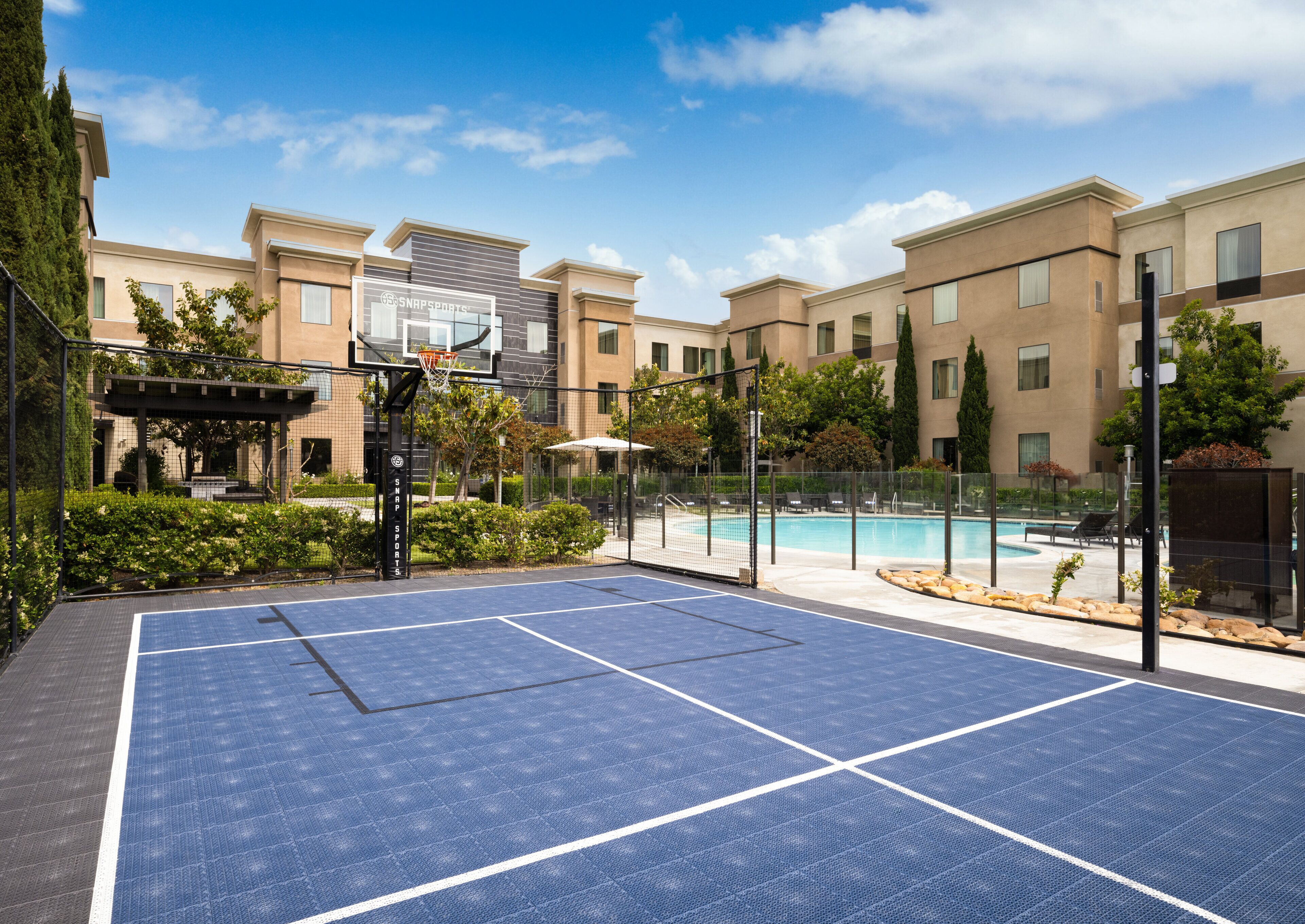 An outdoor basketball court with a pool and lounge chairs in the background.