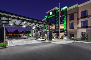 Holiday Inn -hotelli, jossa on katettu sisäänkäynti, ulkoparkkipaikat ja hyvin valaistu julkisivu.