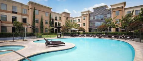 A swimming pool with lounge chairs and a basketball court, surrounded by multi-story buildings.