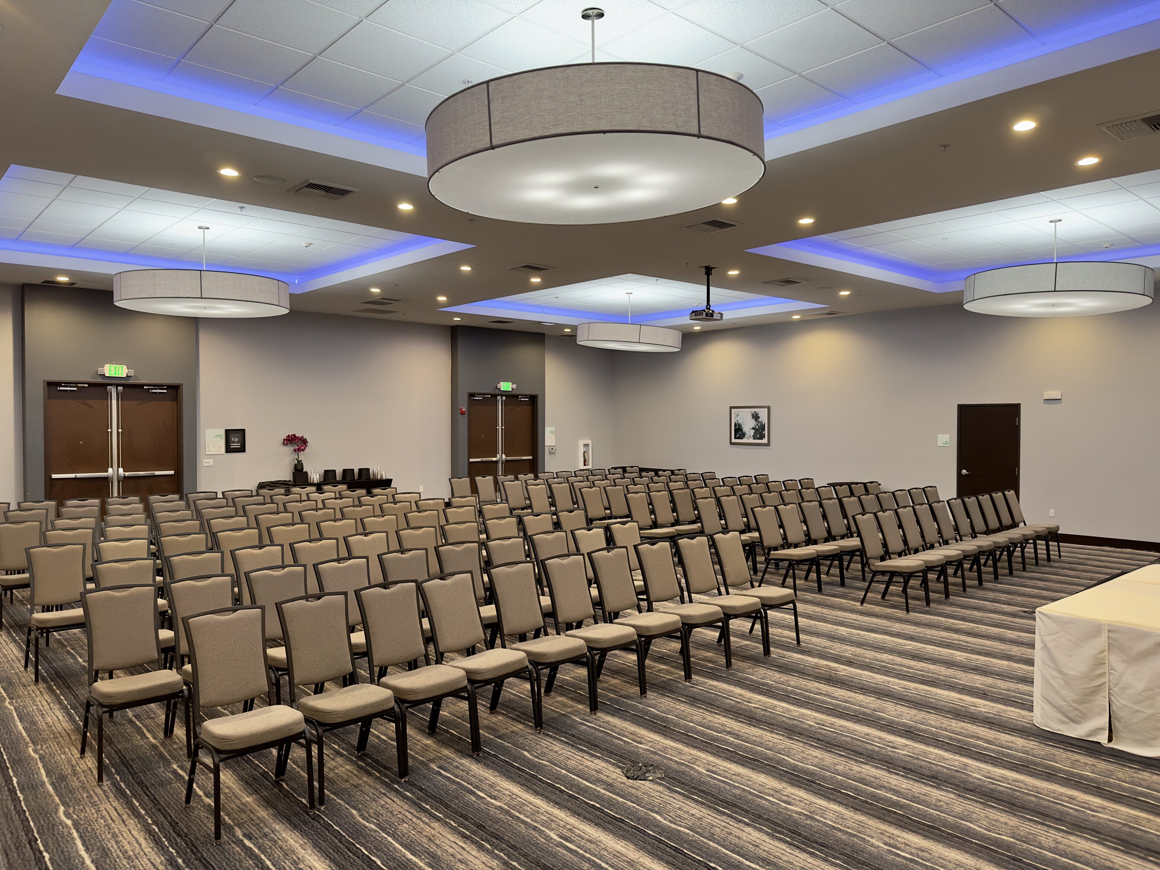 A conference room with rows of chairs, a stage, and a carpeted floor.