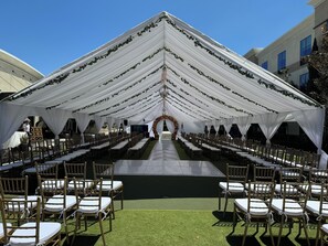 Een tentlocatie buiten de deuren, met rijen stoelen en tafels, een podium aan de voorzijde en een decoratieve boog.
