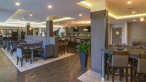 A modern hotel lobby with a bar area, seating arrangements, and a large potted plant. - Holiday Inn Carlsbad by IHG (Carlsbad)