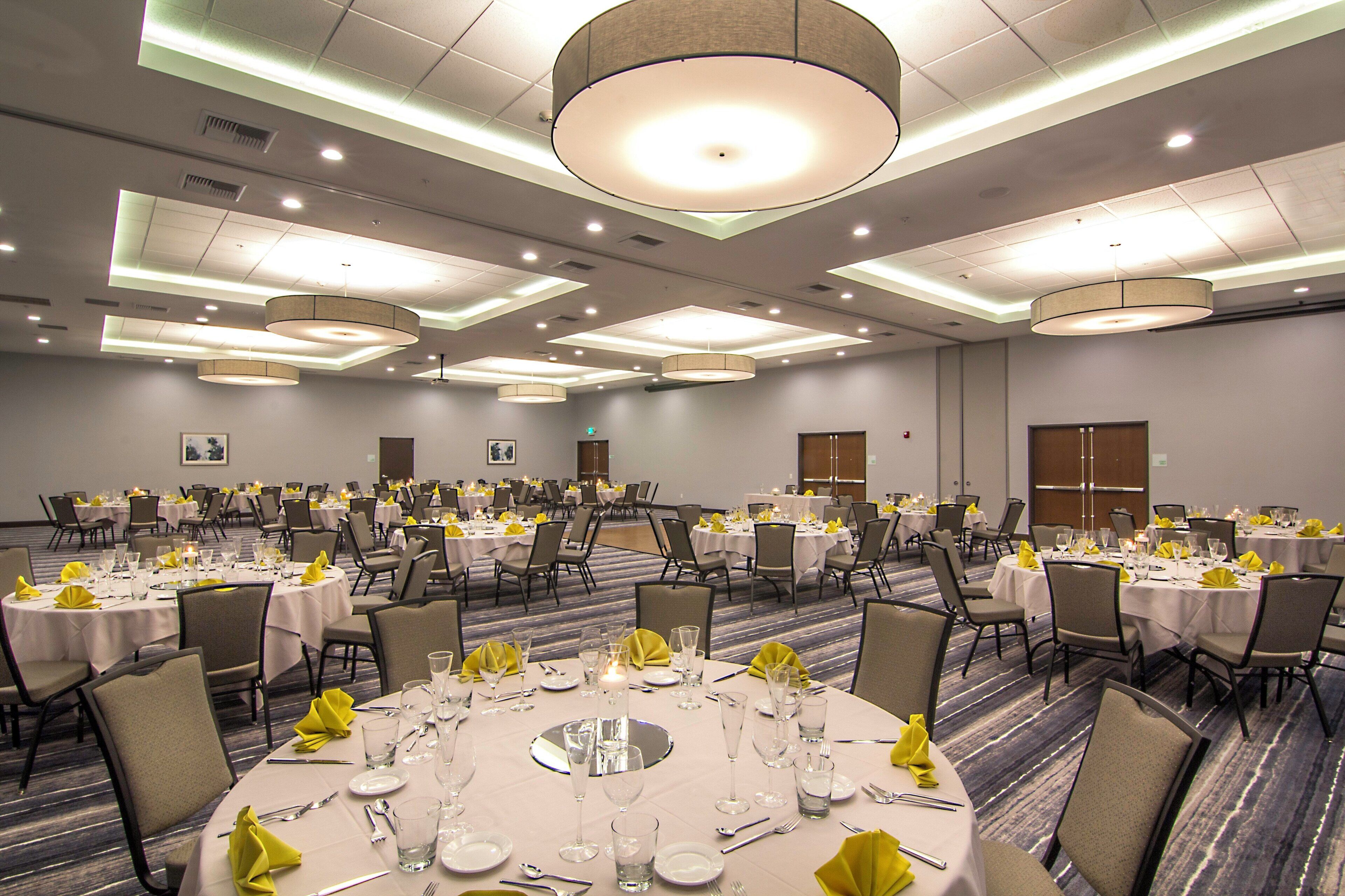 A large banquet hall with multiple round tables set for dining, equipped with chairs and table settings.