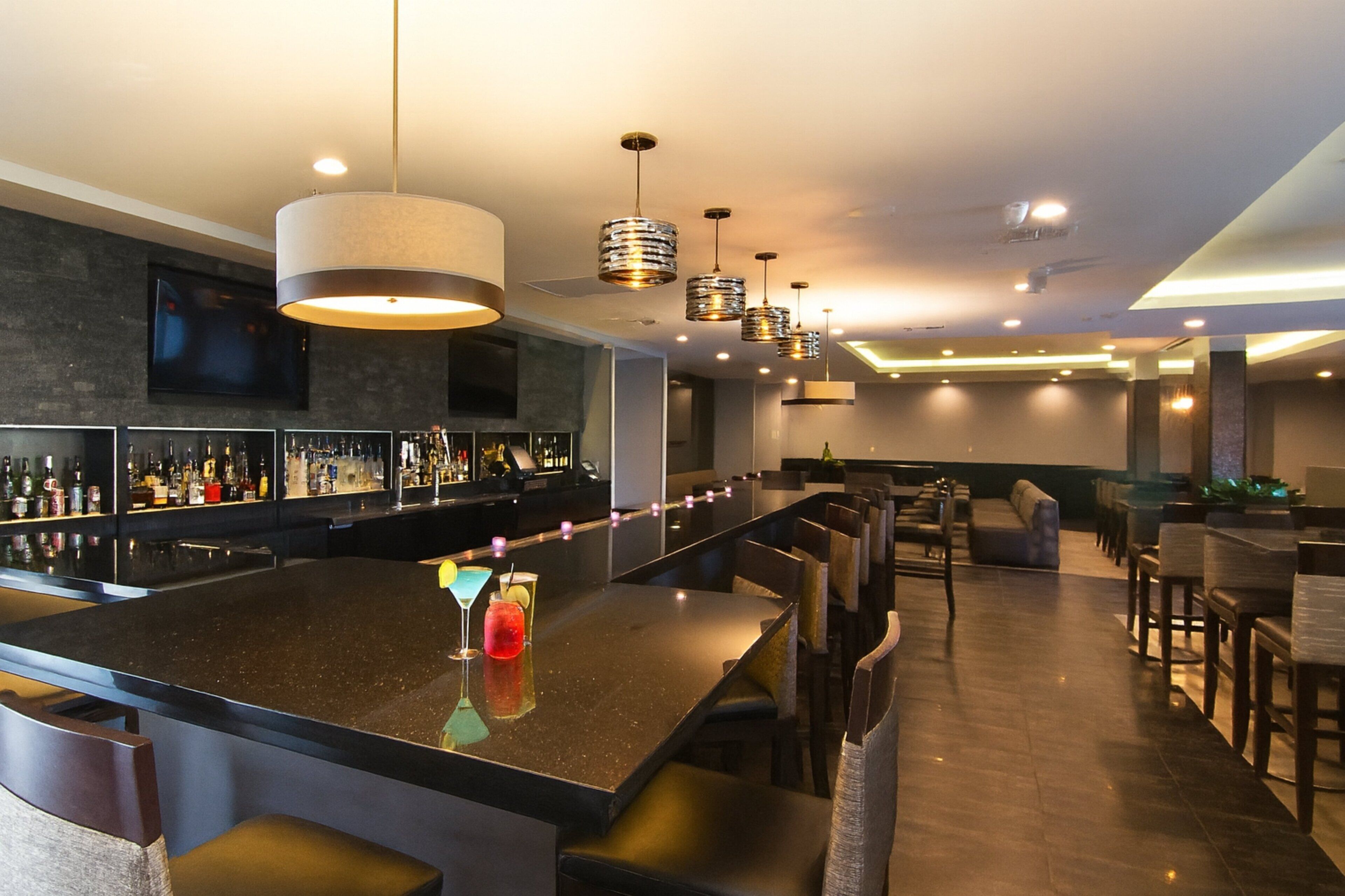 A bar area with a long counter, multiple seating options, and a television mounted on the wall.