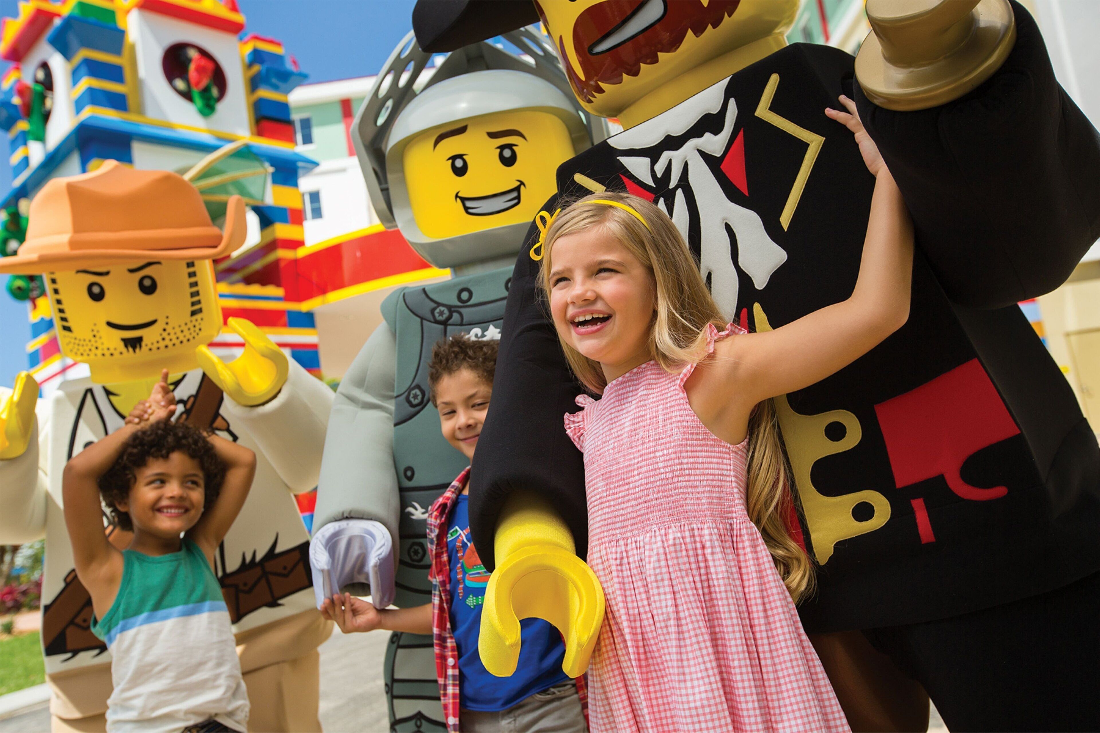 Ryhmä lapsia ja aikuisia värikkään rakennuksen edessä, ja rakennuksen teemana on LEGO.