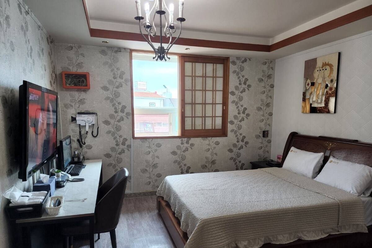 Un dormitorio con cama, escritorio, silla y ventana.