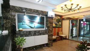 A lobby with a TV mounted on a marble wall, a chandelier, and two seating areas with potted plants. - Andong Hotel (Andong)