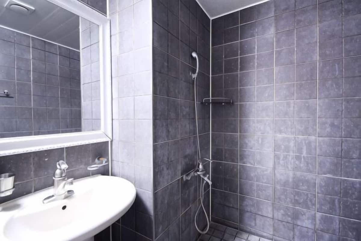 Un baño con lavamanos blanco, un espejo y una ducha con azulejos oscuros.