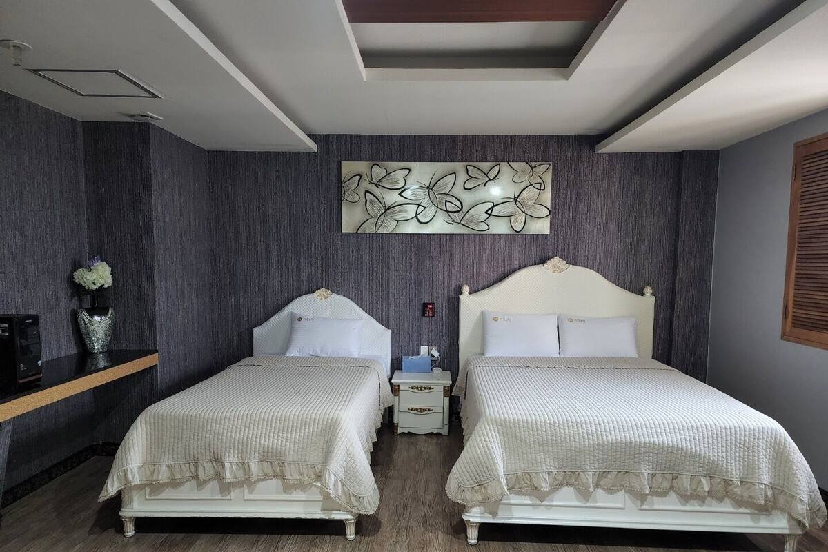 Habitación de hotel con dos camas, una mesita de noche, un jarrón con flores y una obra de arte en la pared.