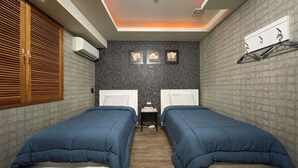 A bedroom with two beds, a wooden wardrobe, a small table, and a wall-mounted drying rack. - Andong Hotel (Andong)
