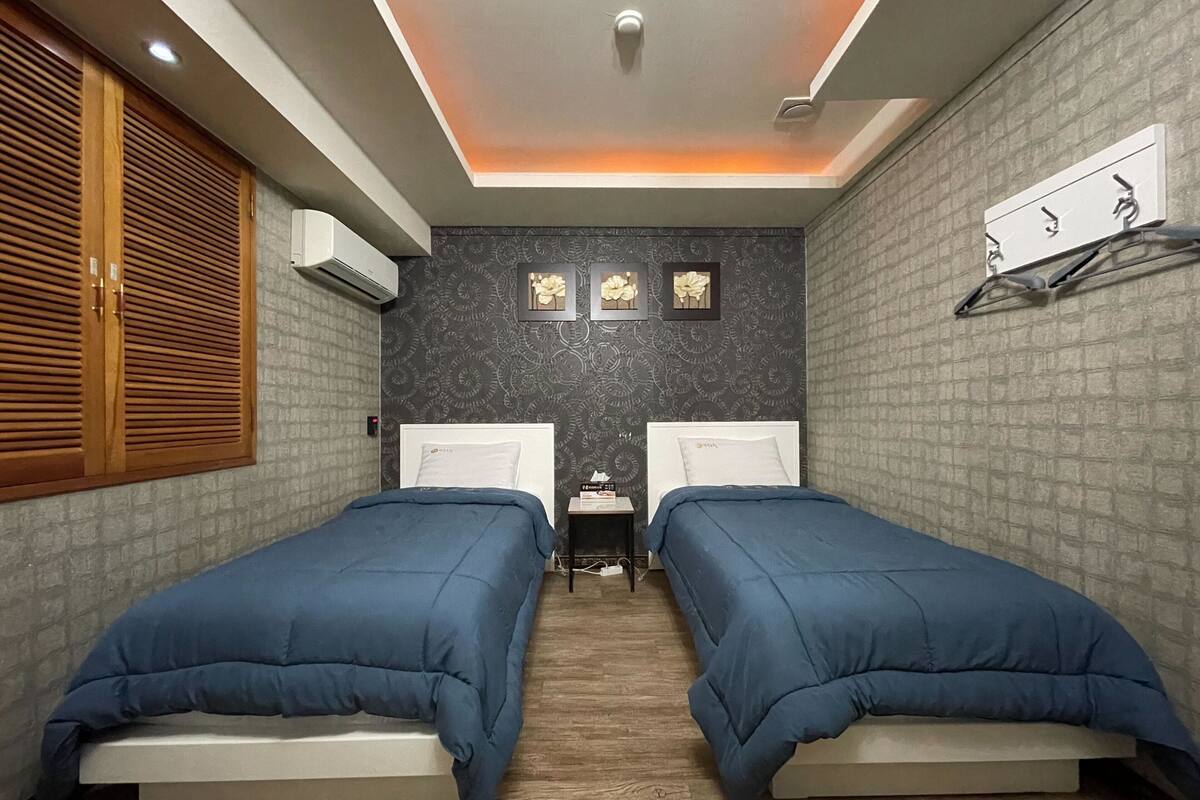 Un dormitorio con dos camas, un armario de madera, una mesita pequeña y un tendedero de pared.