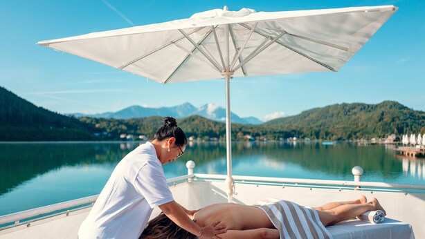 A massage therapy session on a boat with a lake and mountains in the background.