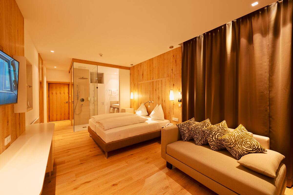 Habitación de hotel con cama, sofá, televisión y zona de ducha.