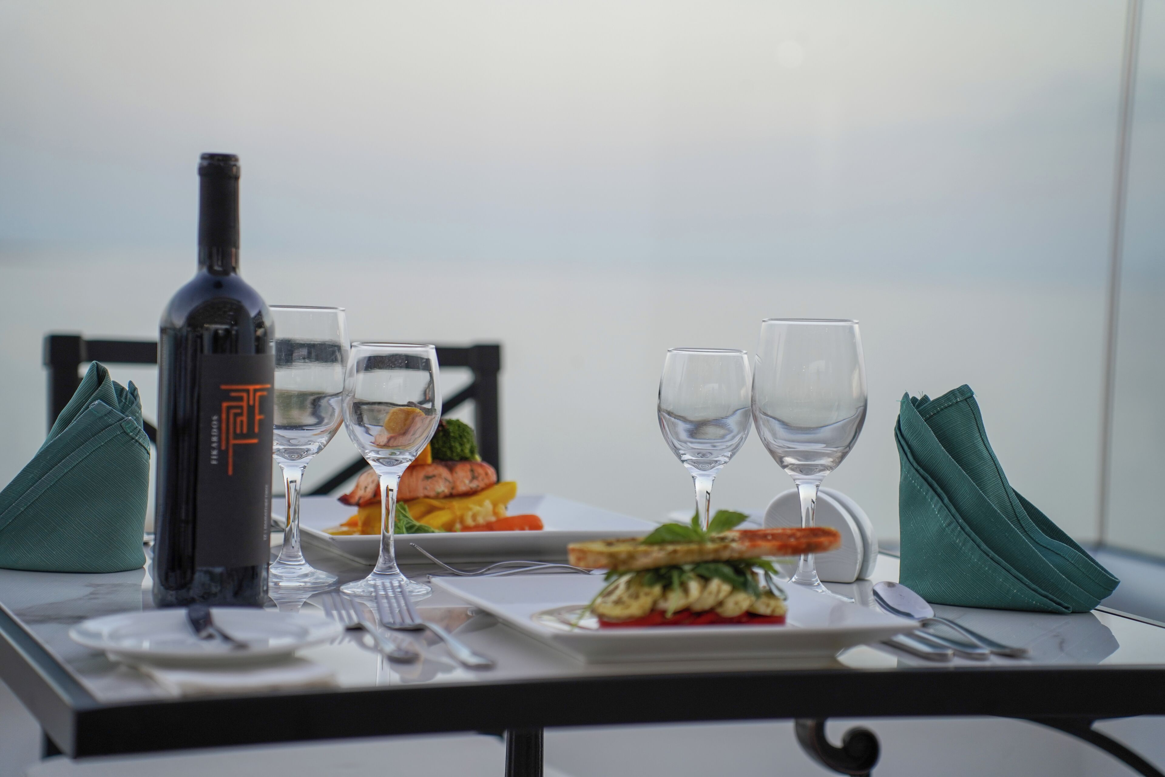 A table set with a bottle, two wine glasses, a plate of food, and a napkin.