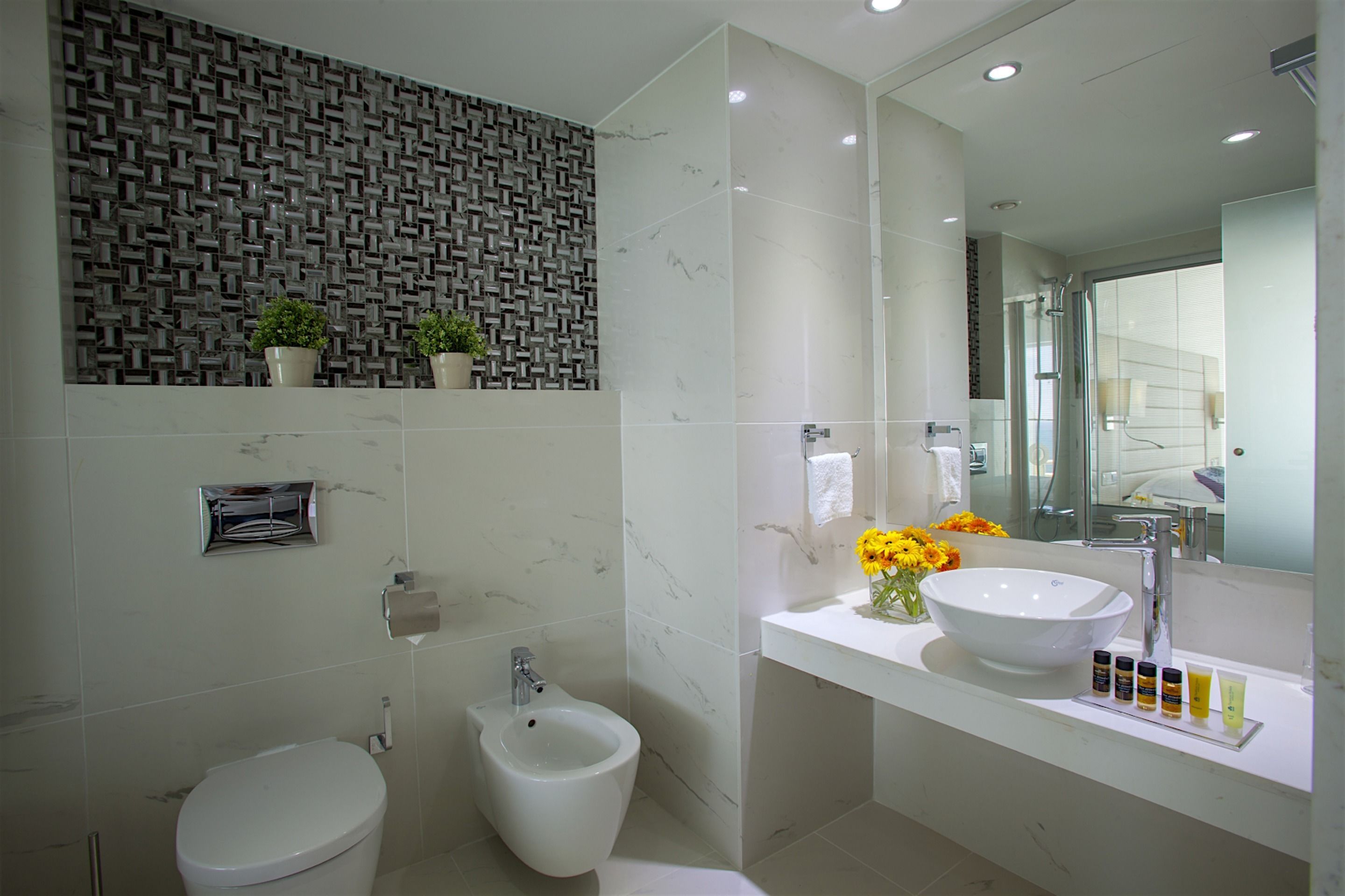 A modern bathroom with a bidet, a large mirror, and a sink with toiletries.