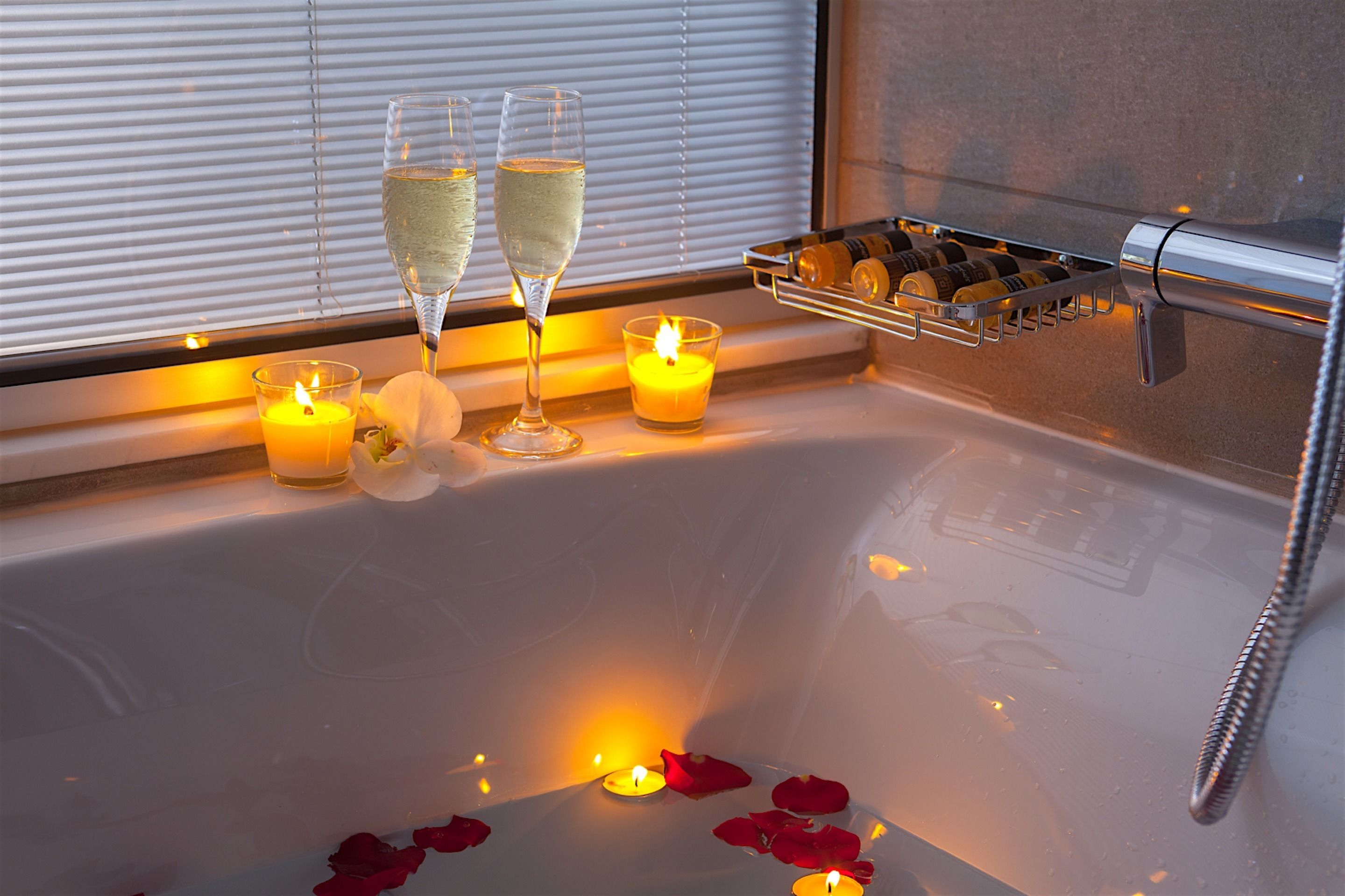 A bathtub with candles, rose petals, and champagne glasses.