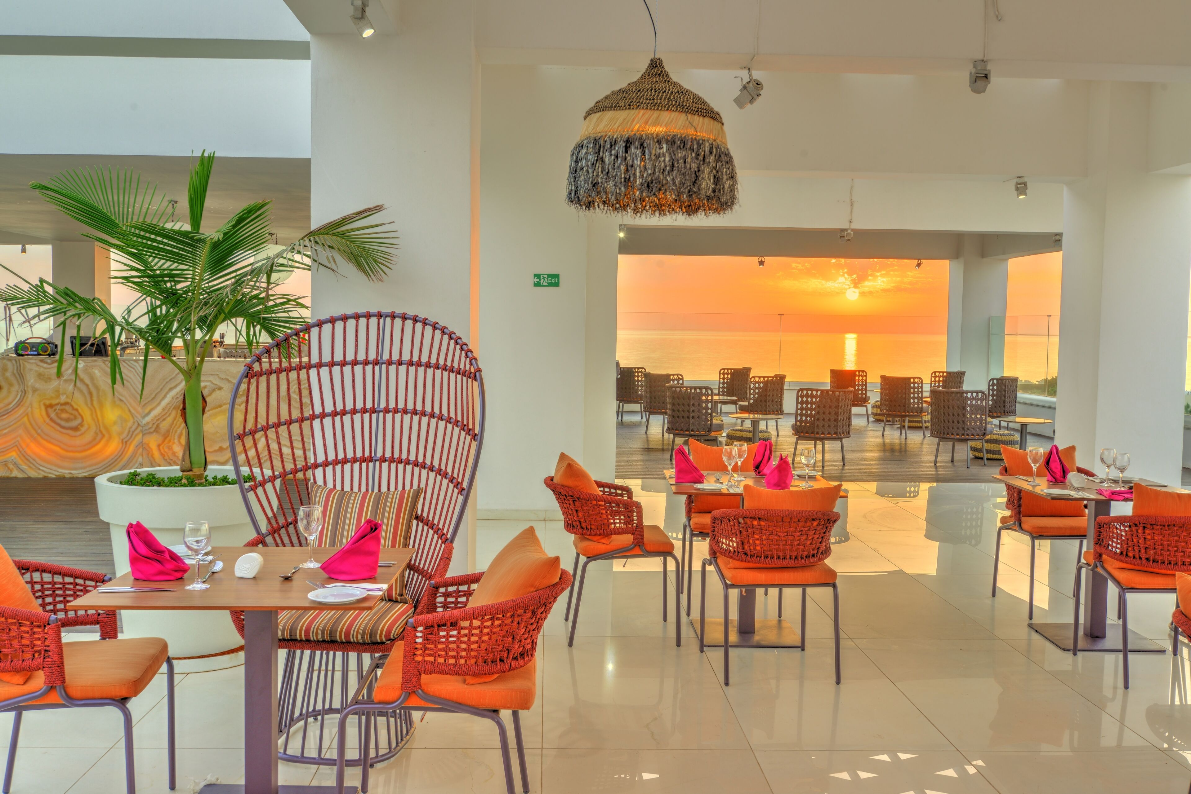 A restaurant with outdoor seating, a large potted plant, and a view of the sunset.