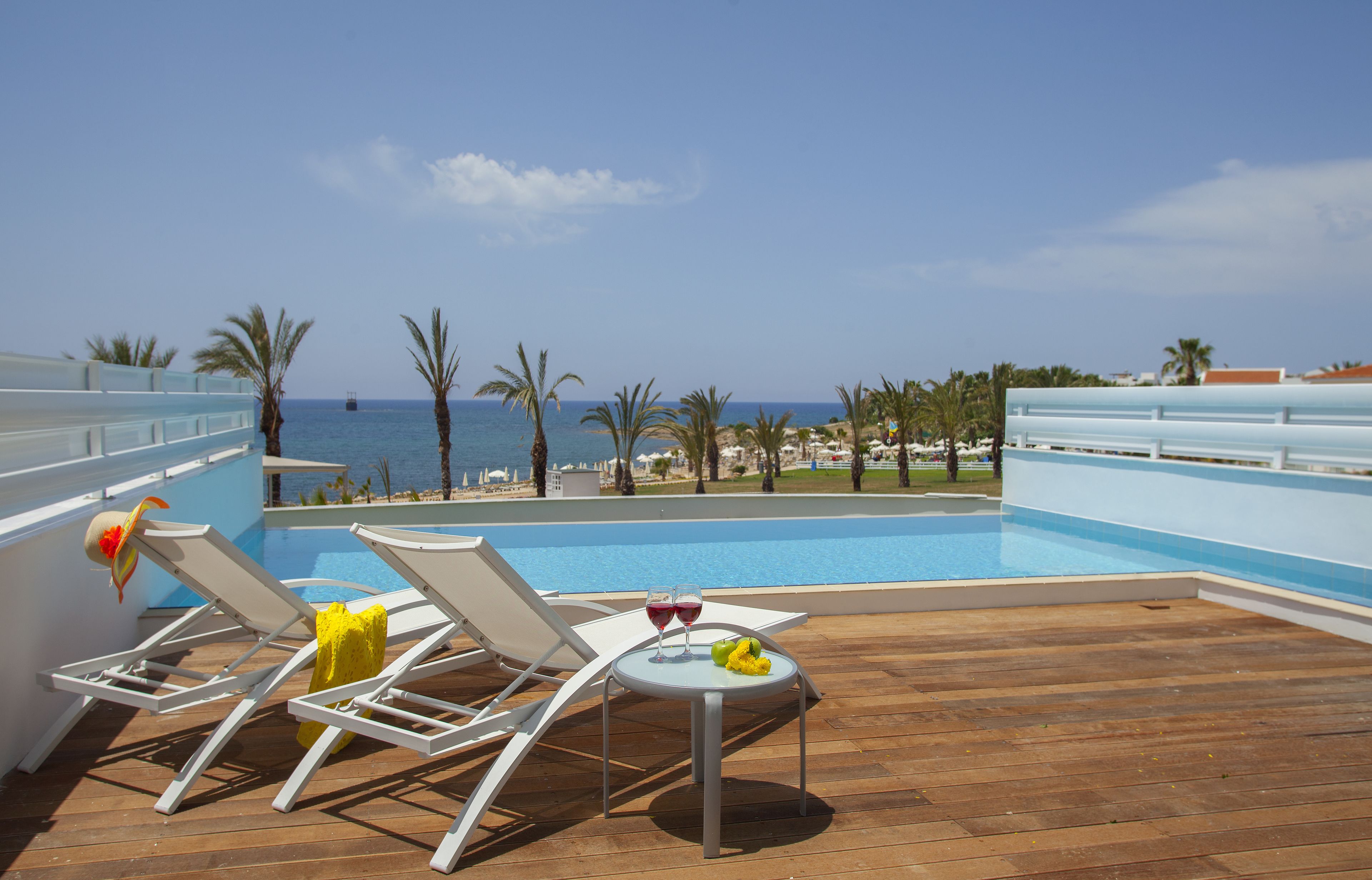 A poolside area with lounge chairs and a table with drinks and fruit, overlooking a beach and ocean.