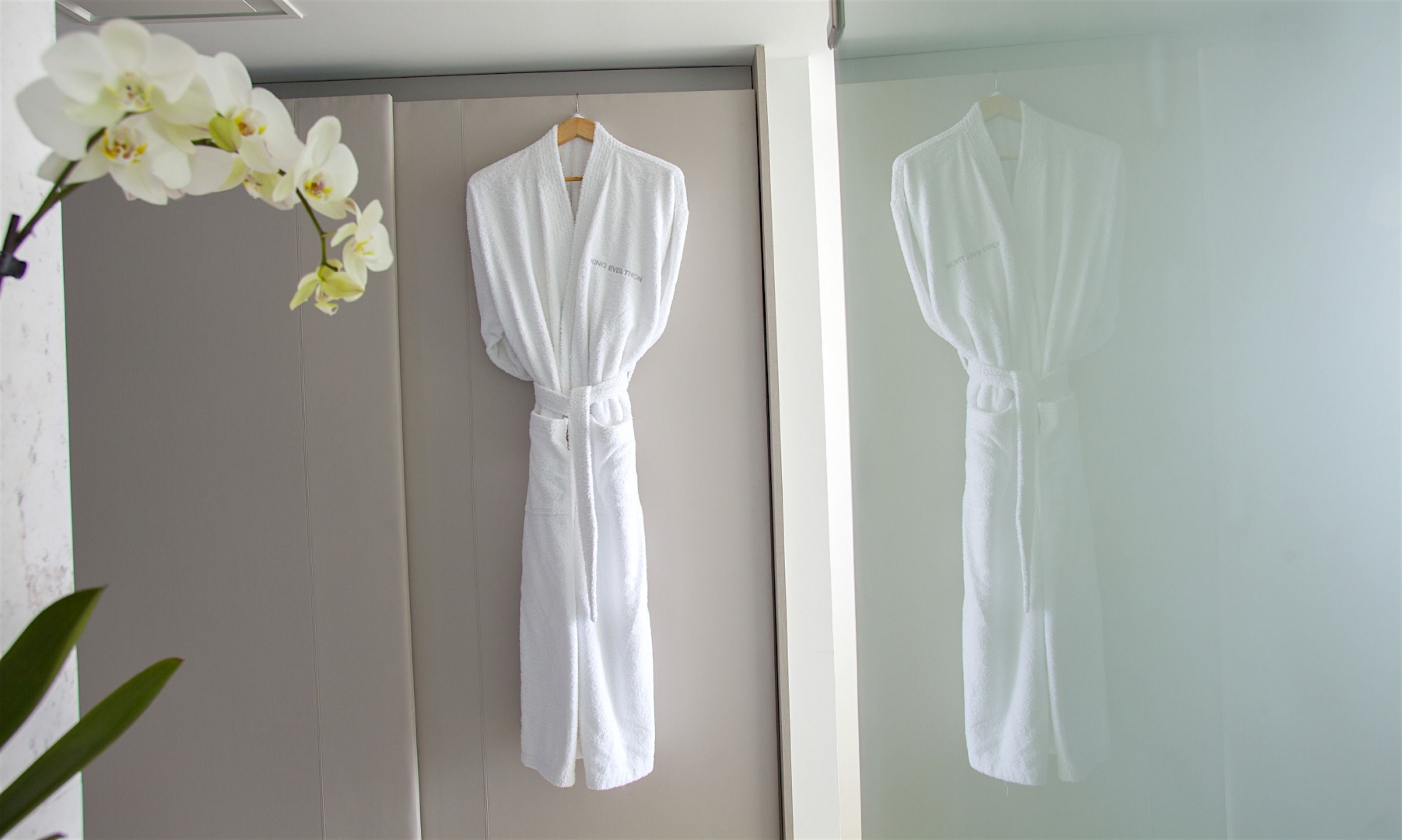 Two white bathrobes hanging on a wall in a bathroom.