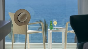 Un balcón con vista al océano, una silla con un sombrero, una mesa pequeña con una botella y una copa.