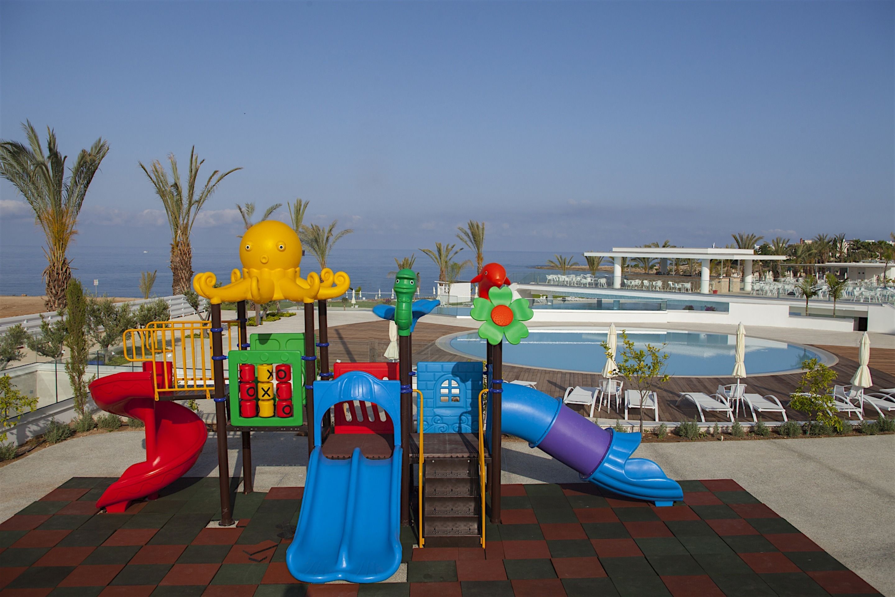 A children's play area with slides and climbing structures, a pool, and lounge chairs.