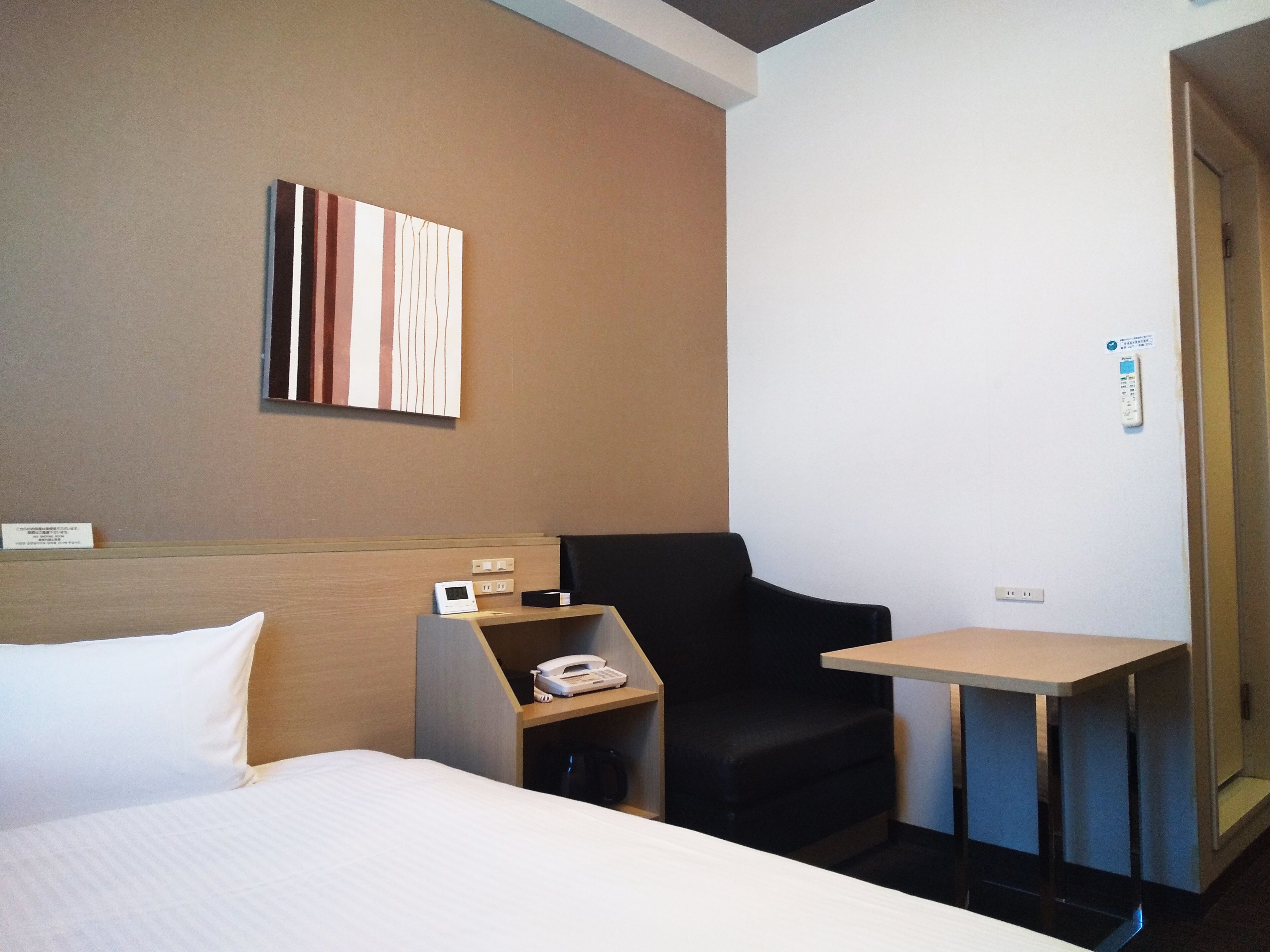 A hotel room with a bed, a desk with a phone, a chair, and a small table.