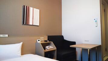 A hotel room with a bed, a desk with a phone, a chair, and a small table.
