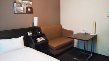 A hotel room with a bed, a desk with a telephone, a lamp, and a small table.