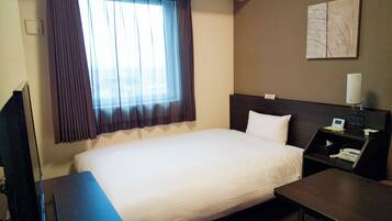 Habitación de hotel con una cama grande, una mesita de noche con lámpara, un televisor y una ventana con cortinas.