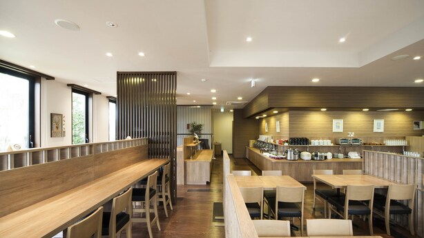 Un restaurante moderno con mesas y sillas de madera, un mostrador con diversos alimentos y una pared decorativa con listones verticales.