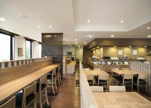 A modern restaurant with wooden tables and chairs, a counter with various food items, and a decorative wall with vertical slats. - Hotel Route Inn Ono (Ono)