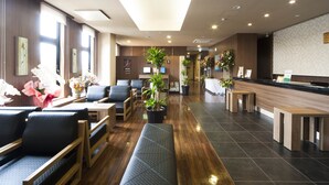 Un vestíbulo de hotel con áreas de estar, un mostrador de recepción y plantas en macetas.