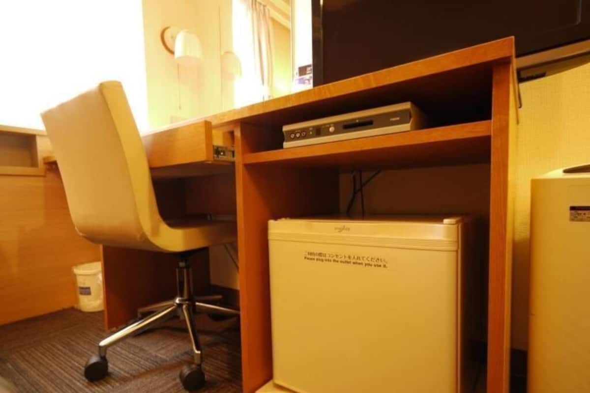 Une chambre d’hôtel équipée d’un bureau, d’une chaise et d’un petit appareil électroménager blanc, peut-être un mini-réfrigérateur.