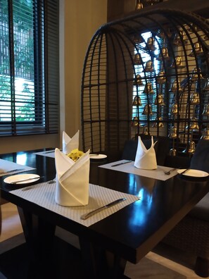Una mesa de comedor dispuesta con servilletas blancas, platos y cubiertos, con una estructura metálica decorativa al fondo.