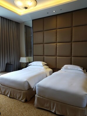 Habitación de hotel con dos camas, un cabecero grande y acolchado, una lámpara y una alfombra estampada.