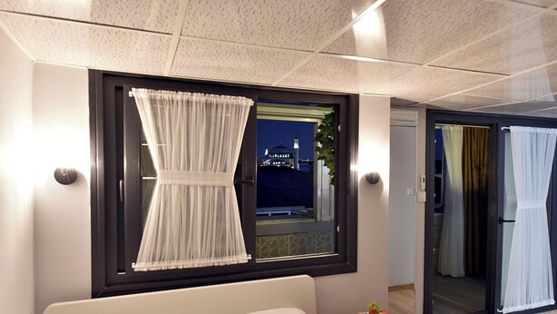 A hotel room with a bed, a small table with fruit, a window with curtains, and a view of a building at night. - Sunlife Hotel Old City (Istanbul)