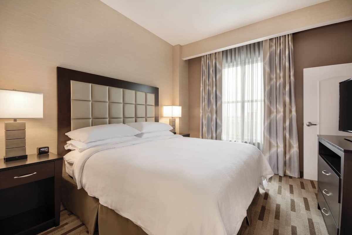 A hotel room with a large bed, bedside lamps, a television, and a wardrobe.