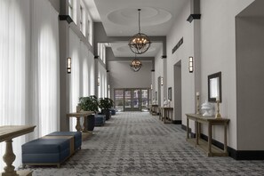 A hotel corridor with a patterned carpet, seating areas, chandeliers, and wall sconces. - Embassy Suites by Hilton Tuscaloosa Alabama Downtown (Tuscaloosa)